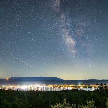 A photo of Big Bear Lake's night sky, the stars are shining brightly amongst a meteor leaving a trail next to a galaxy.