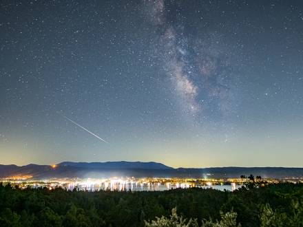 A photo of Big Bear Lake's night sky, the stars are shining brightly amongst a meteor leaving a trail next to a galaxy.