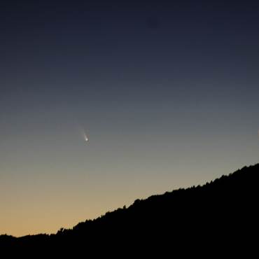 A photo of a silhouetted mountain, the moon is in a waning crescent stage as a comet is passing far away.