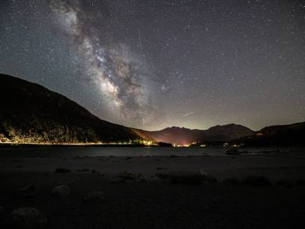 A photo of Big Bear's Night Sky - the milky way galaxy along with many stars are visible above the gently lit mountains.