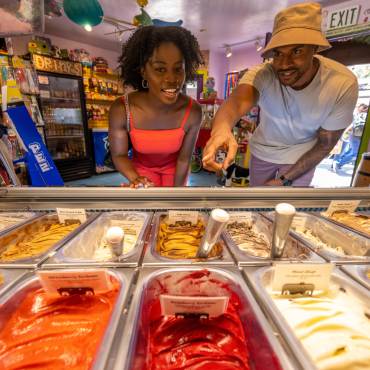 A couple peers through glass at a selection of colorful gelato flavors at a sweet shop in The Village at Big Bear Lake, CA.