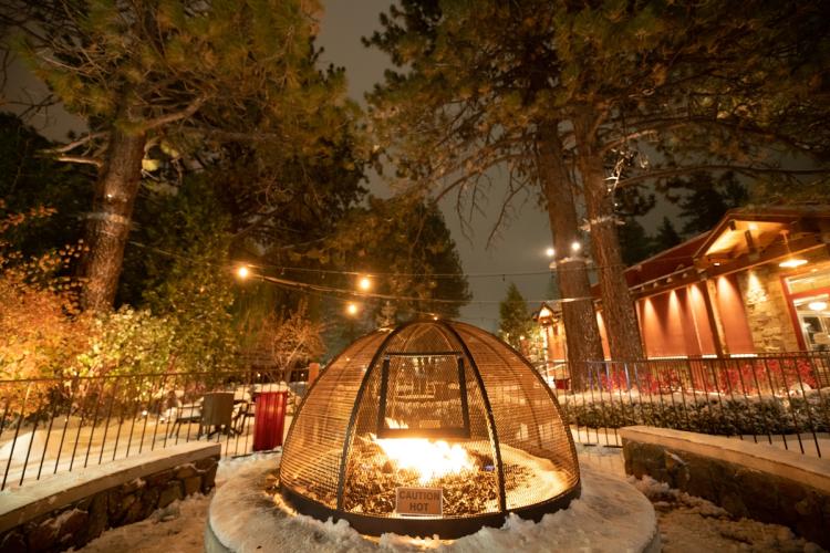 A photo of a fire pit in the Big Bear Lake Village during winter - there some snow across the ground and around the fire pit.
