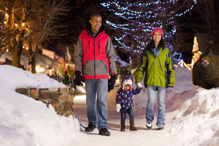 A family strolls through The Village at Big Bear Lake in the winter. Snow is all around them.