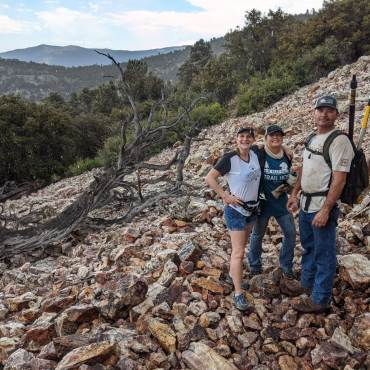 A photo of volunteers on a rocky hill, one of them is carrying a backpack with long tool like sticks.