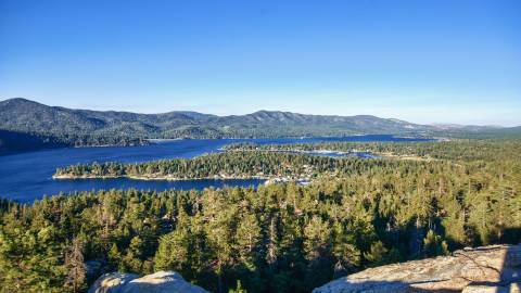 Cliff top view of a forest, lake and mountain range in Big Bear, California, on a sunny day.