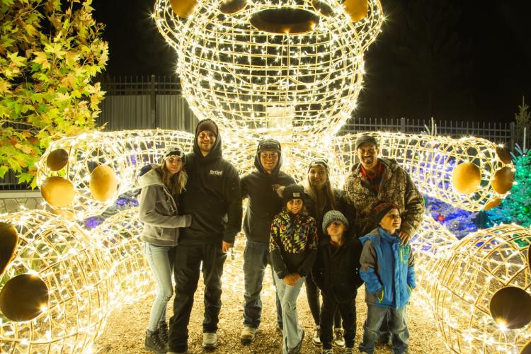 A photo of a family posing for a photo in-front of a large light display, the display looks like a giant teddy bear.