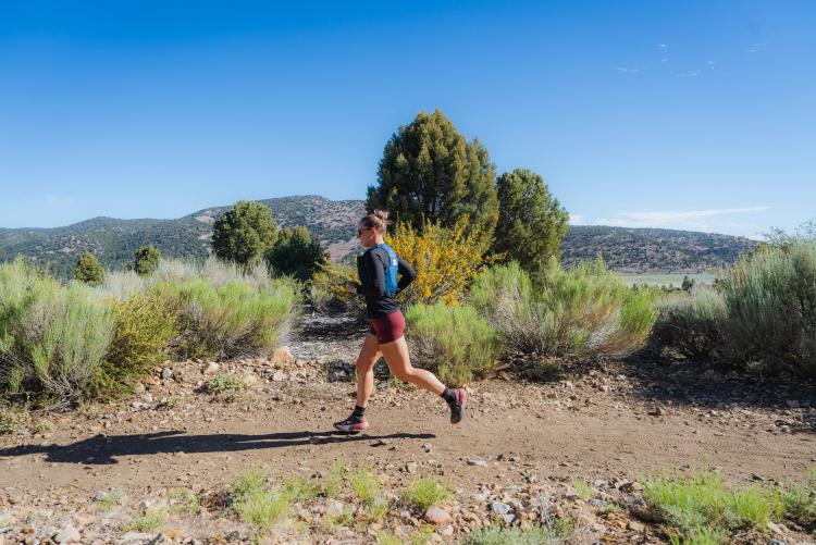 A photo of a female hiker walking along a dirt trail in Big Bear Lake California - the mountains and trees visible behind her