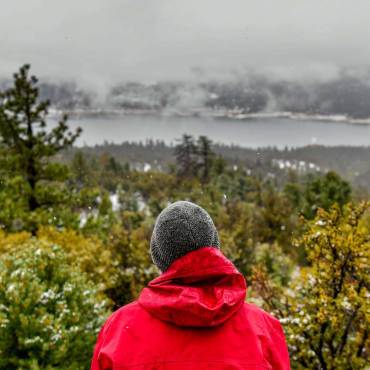 A man gazes out on a winter forest landscape. A frosty lake and rich green forest are sprawled across the landscape.