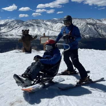 A pair of two skiers getting ready to go down the slopes at Bear Mountain - one of them is using accessibility skis.