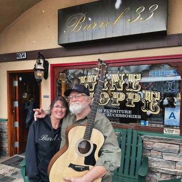 A photo of a man and a woman in front of Barrel 33 - the man is holding an acoustic guitar.