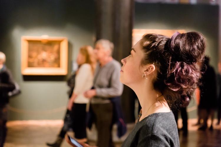 A photo of a female looking up from her phone in the middle of an art gallery.