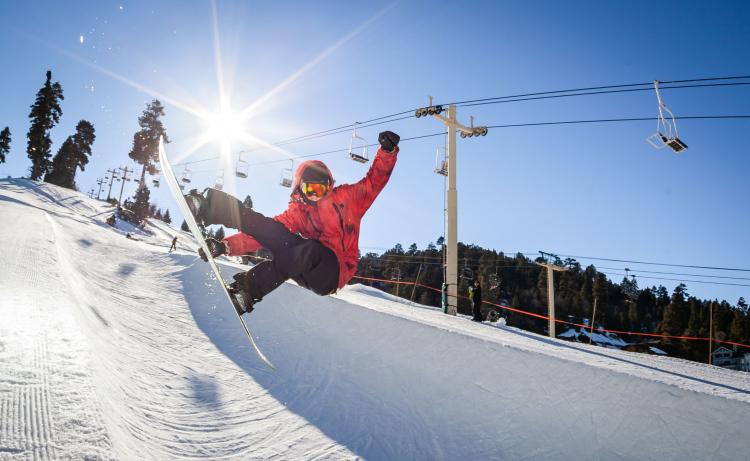 A photo of a snowboarder mid-jump from a half-pipe - the sun is shining behind the person and onto the snow half-pipe.