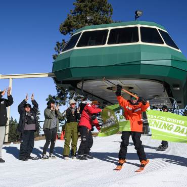 A photo of Bear Mountain Ski Resort's 2025/26 winter season opening day - someone is splitting a banner while wearing skis.