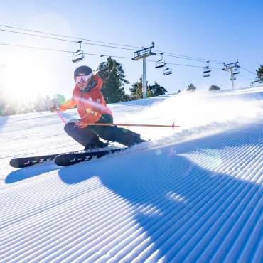 A photo of a skier going down the snow covered slopes with a trail of snow dust behind her - the sun glowing brightly behind.