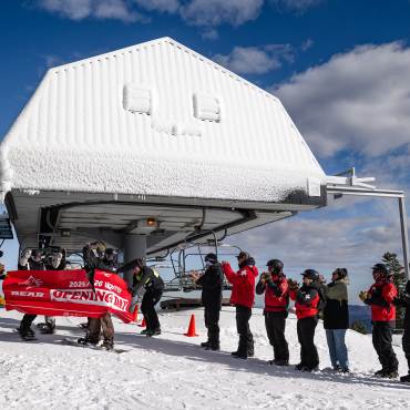 A photo of Bear Mountain Ski Resort's 2025/26 winter season opening day - someone is splitting a banner while wearing skis.