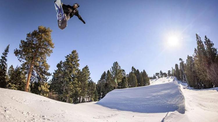 A photo of a snowboarder holding his board mid-air after a jump from a ramp of snow - the sun brightly shining in behind.