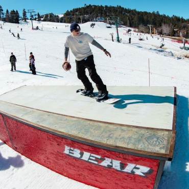 A photo of a snowboarder going up a ramp while holding a football during the Bear Bowl X event, there is a large crowd behind