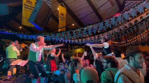 A large crowd gathered for a live band playing on stage at Oktoberfest - one musician is reaching out to someone in the crowd