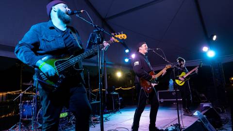 A band playing on stage during the MX Grand Prix - they are playing on guitars while singing into microphones.