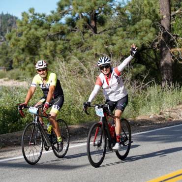 Two cyclists wave during their Tour de Big Bear bike ride in Big Bear Lake, CA