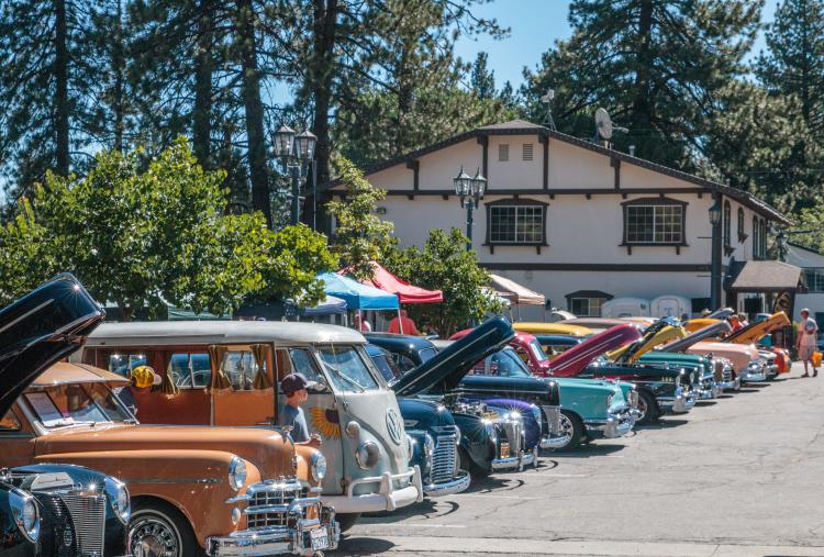 Shiny and multi-colored antique cars fill a parking lot for the Big Bear Lake Fun Run. The hoods are lifted for spectators.