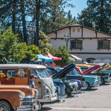Shiny and multi-colored antique cars fill a parking lot for the Big Bear Lake Fun Run. The hoods are lifted for spectators.