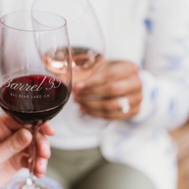 A photo of two people's hands holding a glass of wine with the logo of Barrel 33.