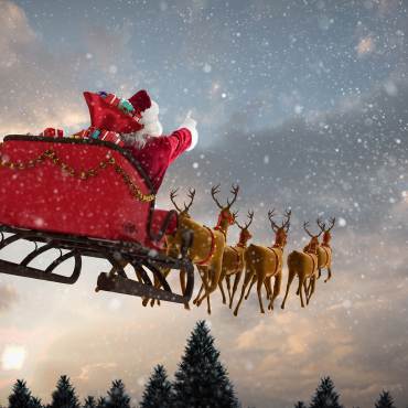 A picture of Santa riding his red sleigh pulled along by his reindeer through the falling snow, the sun beginning to rise.
