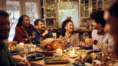 A large group of people sitting at a long dinner table with food during Thanksgiving - they are smiling and laughing.