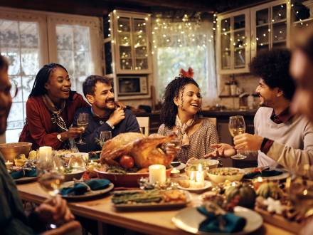 A large group of people sitting at a long dinner table with food during Thanksgiving - they are smiling and laughing.