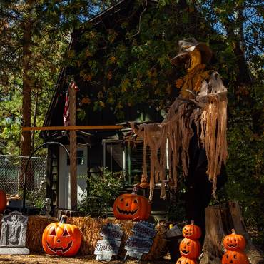 A 2026 Big Bear Scarecrow & Dia de Los Muertos competition display - there is a giant scarecrow beside graves and pumpkins.