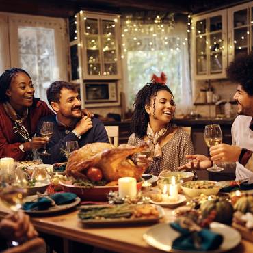 A large group of people sitting at a long dinner table with food during Thanksgiving - they are smiling and laughing.