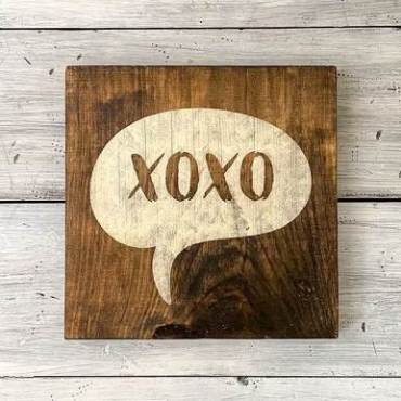 A wooden sign painted with XOXO sits on a white background.