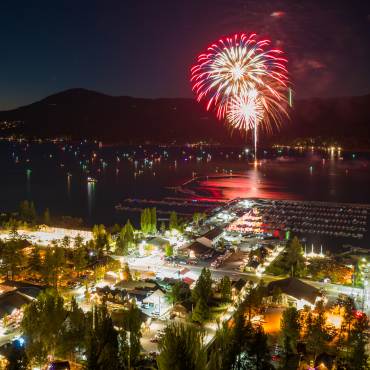 A red firework explodes above Big Bear Lake on the 4th of July. Boat and city lights are visible in this night scene.