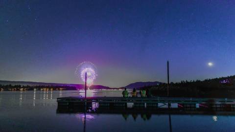 people sit on a dock on Big Bear Lake and admire the 4th of July fireworks show as fireworks reflect off of the lake