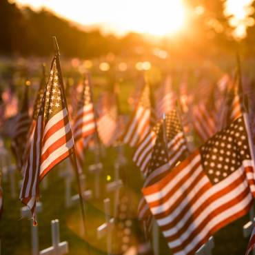 A field of white crosses topped with American Flags honoring fallen soldiers, the sun gently glaring onto the flags.