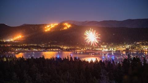Bright fireworks displayed mid-air during Big Bear Lake's 4th of July celebration - the mountains and lake are visible.