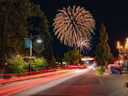 A long exposure of red tail lights in The Village at Big Bear Lake. 4th of July fireworks are visible in the night sky.