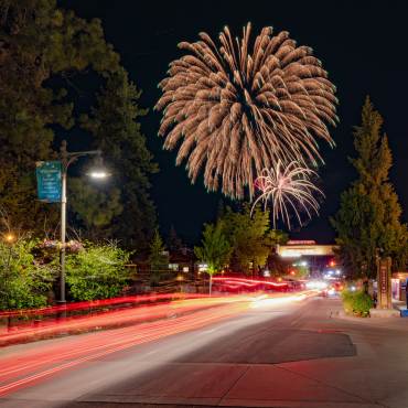 A long exposure of red tail lights in The Village at Big Bear Lake. 4th of July fireworks are visible in the night sky.