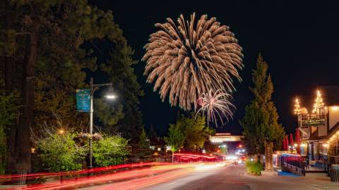 A long exposure of red tail lights in The Village at Big Bear Lake. 4th of July fireworks are visible in the night sky.