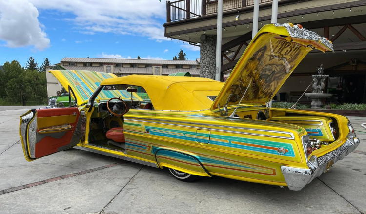 A photo of a lowrider parked in front of the Holiday Inn - the car is yellow with light blue stripes and a soft top.