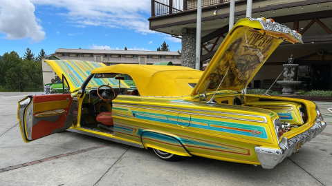 A photo of a lowrider parked in front of the Holiday Inn - the car is yellow with light blue stripes and a soft top.