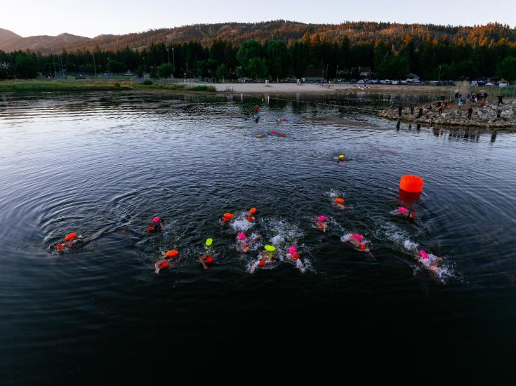 A drone shot taken during LakeFest of participating swimmers, the water gently reflecting the mountains in the background.