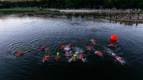 A drone shot taken during LakeFest of participating swimmers, the water gently reflecting the mountains in the background.