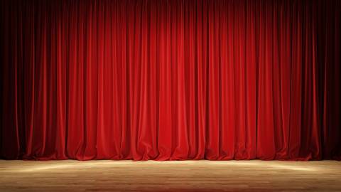 A photo of red stage curtains closed, the spotlights aimed at the center gently illuminating the wooden stage underneath.