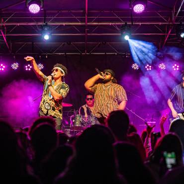 A photo taken from the crowd at the Summer Concert Series, the four band members playing their instruments and singing.