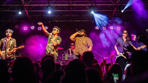 A photo taken from the crowd at the Summer Concert Series, the four band members playing their instruments and singing.