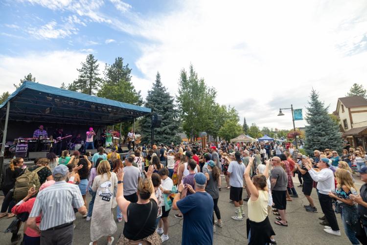 A photo taken during the Summer Concert Series, the band is playing on stage in front of a large crowd located in the Village