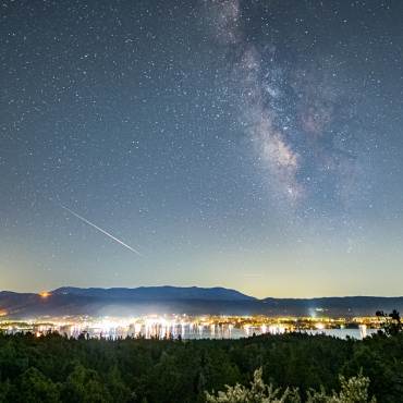 A wide far away view of Big Bear Lake at night - the milky way and stars are visible above the town and lake below.