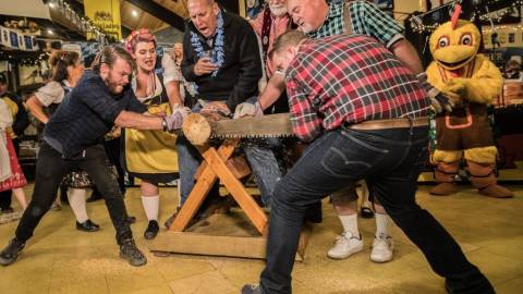People cheer on as two men use a two-person saw to cut through a log in the log sawing competition at Oktoberfest